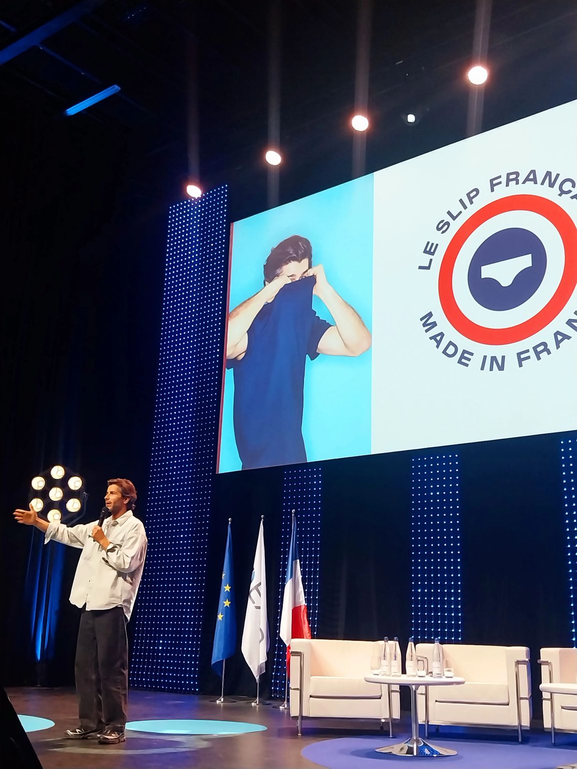 Guillaume Gibault sur scène, micro en main, devant un écran géant aux couleurs du Slip Français